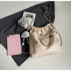 Detail of beige drawstring bucket bag with leather heart patches and plush cloud charm