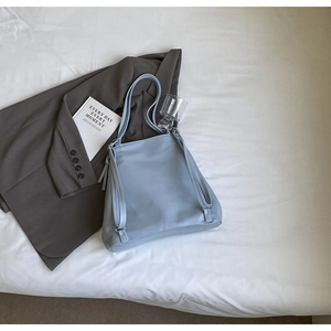 Détail d'un sac à dos minimaliste bleu clair en cuir souple sur un tissu blanc texturé