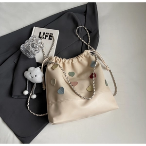 Detail of cream drawstring bucket bag with colorful heart patches and plush cloud charm