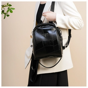 Detail of black patchwork backpack with metal triangle badge worn over white business suit