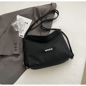 Detail of black textured shoulder bag featuring four silver metal heart-shaped ornaments