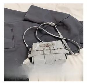 Detail of light grey pleated shoulder bag featuring a rhinestone bow and plush charm