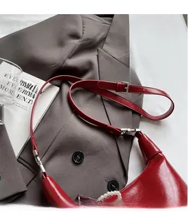 Gros plan du sac croissant en cuir rouge avec chaîne en perles sur un costume gris