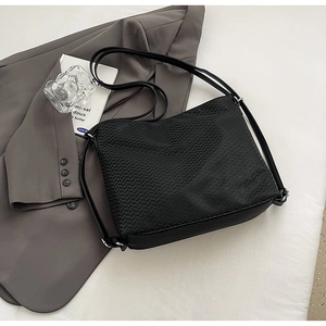 Detail of black crossbody bag with chevron texture and adjustable strap on a blazer
