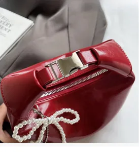 Détail du sac à main rouge en cuir verni avec poignée argentée et breloque perle