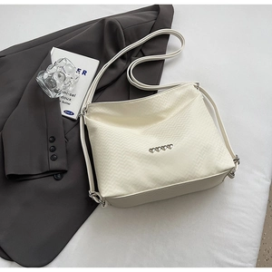 Detail of cream shoulder bag featuring V-shaped woven texture and silver heart accents