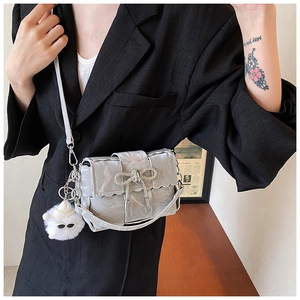 Detail of silver pleated crossbody bag with rhinestone bow and plush monster charm