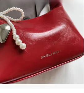Détail du sac à main rouge en cuir texturé avec bandoulière perlée et breloque cœur