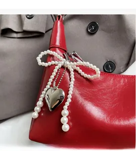 Détail du sac en cuir rouge avec nœud en perles et pendentif cœur argenté élégant