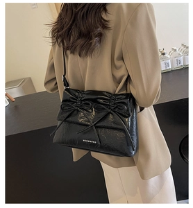 Model view of black glossy pleated shoulder bag with delicate double bow details