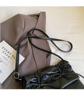 Close-up of black pleated ballet style shoulder bag with ribbon bow and long strap