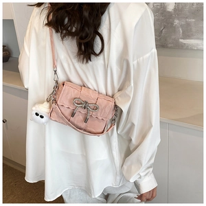 Detail of pink pleated crossbody bag with woven bow and cute plush eye charm on a white shirt