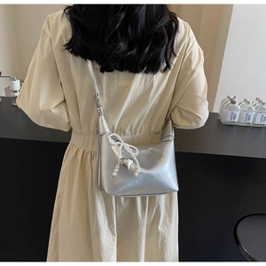 Détail du sac à bandoulière argenté avec nœud en perles et breloque cœur sur une robe