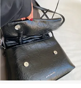 Detail shot of the glossy black pleated crossbody bag with magnetic snap closure