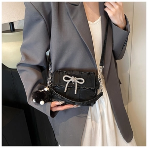 Detail of black woven shoulder bag featuring a rhinestone bow and plush ball charm