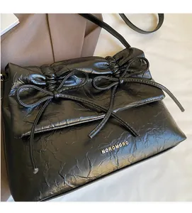 Detail of black pleated shoulder bag featuring elegant ribbon bows and metal brand logo