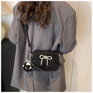 Detail of black glossy handbag with sparkling rhinestone bow and plush ball charm