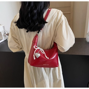 Détail d'un sac bandoulière en cuir rouge avec nœud en perles et pendentif cœur argenté