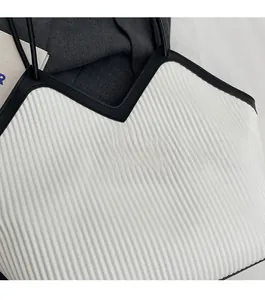 Detailed close-up of white pleated tote bag with black trim and Fashion emblem logo