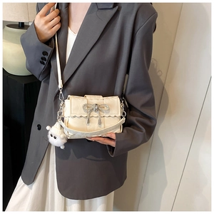 Detail of beige woven mini bag featuring a rhinestone bow and wave-cut flap cover