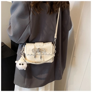 Close-up of beige woven crossbody bag featuring a rhinestone bow and plush lamb charm