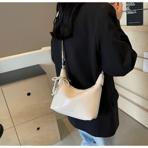 Détail du sac hobo crème avec nœud en perles et logo SHELLKYP sur un blazer noir