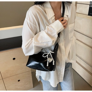 Détail d'un sac porté épaule en cuir noir brillant avec nœud perlé et pendentif cœur