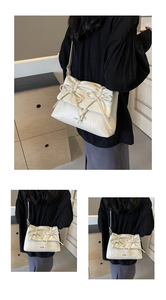 Detail of cream white pleated shoulder bag featuring elegant bow accents and soft texture