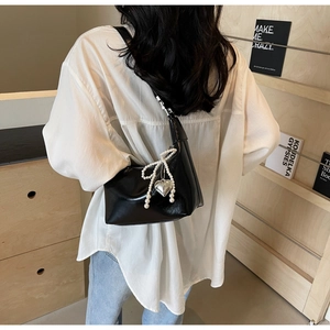 Détail du sac croissant en similicuir noir avec nœud en perles et pendentif cœur argenté