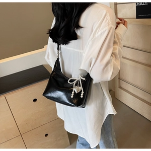 Détail du sac en cuir verni noir avec nœud en perles et breloque en forme de cœur