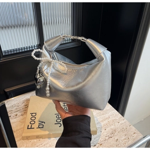 Détail du sac à main argenté métallisé avec breloque nœud en perles et pendentif cœur