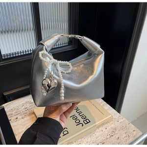 Détail du sac argenté avec pendentif nœud en perles et cœur sur fond de marbre
