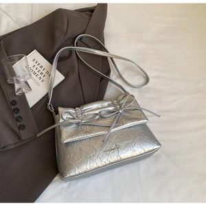 Detailed view of silver metallic pleated crossbody bag with dual bow accents and logo
