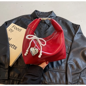 Détail d'un sac à main rouge brillant avec fermoir argenté et breloque noeud en perles
