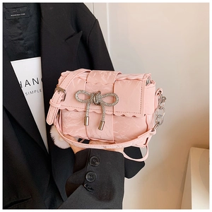 Close-up of pink woven crossbody bag with diamond bow and plush ball keychain detail
