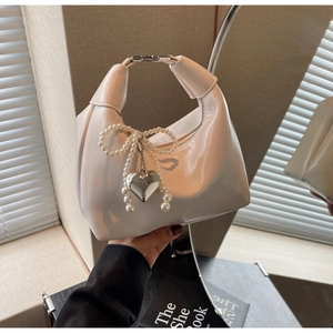 Détail d'un sac à main crème en cuir avec nœud en perles et pendentif cœur argent
