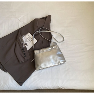 Close-up of a metallic silver flap shoulder bag on a stylish brown suit background