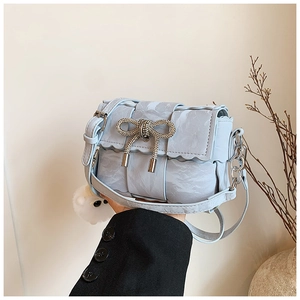 Close-up of light blue woven bag with rhinestone bow and wave-edge flap detail