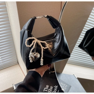 Détail du sac demi-lune en cuir verni noir avec nœud en perle et pendentif cœur argenté
