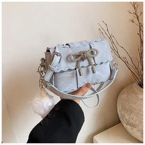 Close-up of light blue woven crossbody bag with rhinestone bow and plush charm