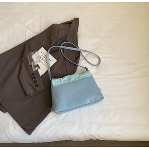 Overhead view of light blue leather shoulder bag on beige fabric and brown blazer