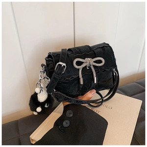 Detail of black velvet mini bag with rhinestone bow and plush charm on leather seat