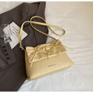 Detail of cream pleated crossbody bag featuring dual bow accents and metal logo detail