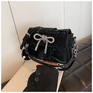 Detail of black pleated crossbody bag with sparkling rhinestone bow and metal chain strap