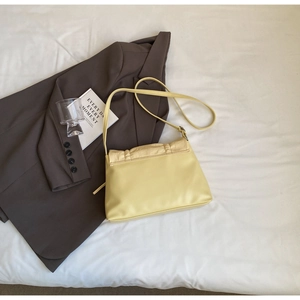 Detail view of the yellow pleated leather shoulder bag on a minimalist fabric background