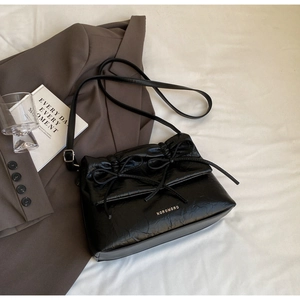 Close-up of black ballet-style shoulder bag featuring elegant bow details and pleated texture