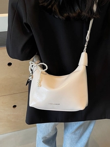 Sac bandoulière minimaliste blanc crème avec breloque perle porté par un modèle