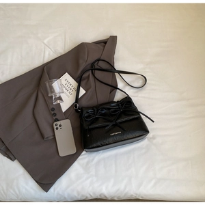Detail of black pleated shoulder bag with bow drawstring and magnetic flap closure
