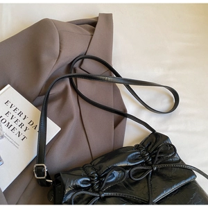 Detail of black wrinkled leather shoulder bag with a bow accent next to a brown suit