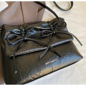 Detail showing black wrinkled leather texture and elegant bows on the stylish handbag